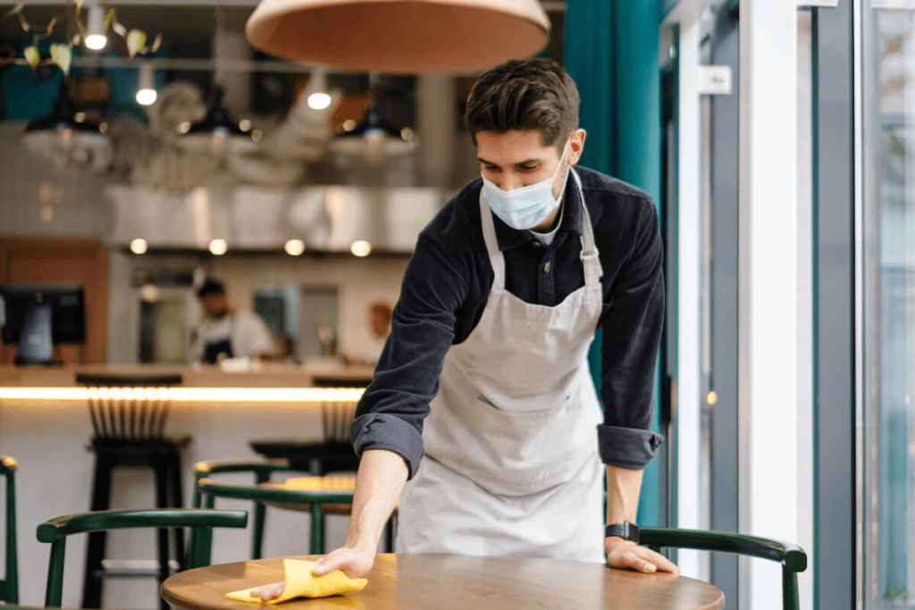 Employee turnover: Waiter in a mask cleans a table